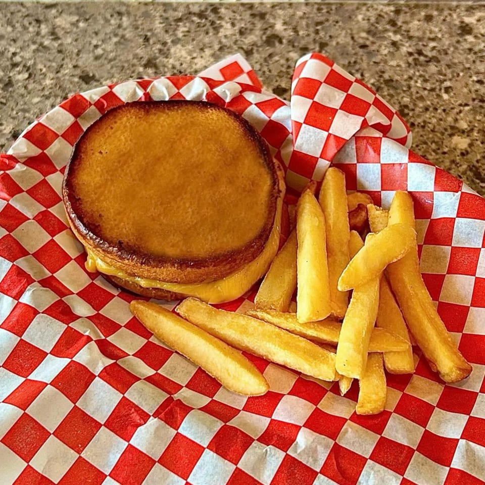 Grilled cheese sandwich with melted cheese and a side of golden fries in a red and white checkered basket.